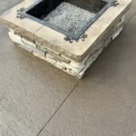Square stone fire pit on patio surface.